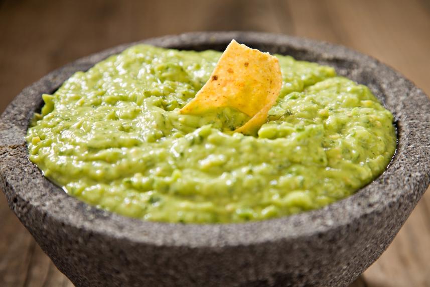 Photo: Tomatillo guacamole and tortilla chip in a stone bowl.