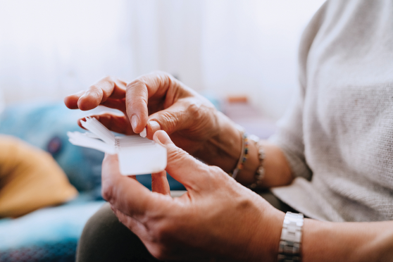 A persons hands, holding a pill container and grabbing a pill